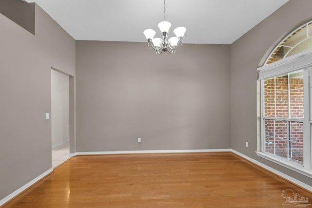 unfurnished room featuring baseboards, an inviting chandelier, and wood finished floors
