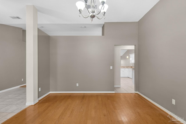 empty room featuring visible vents, baseboards, a notable chandelier, and light wood-style floors