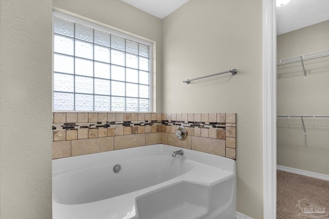 bathroom with baseboards, a walk in closet, and a garden tub