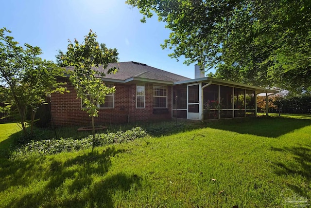 rear view of house with brick siding, a chimney, a sunroom, and a lawn