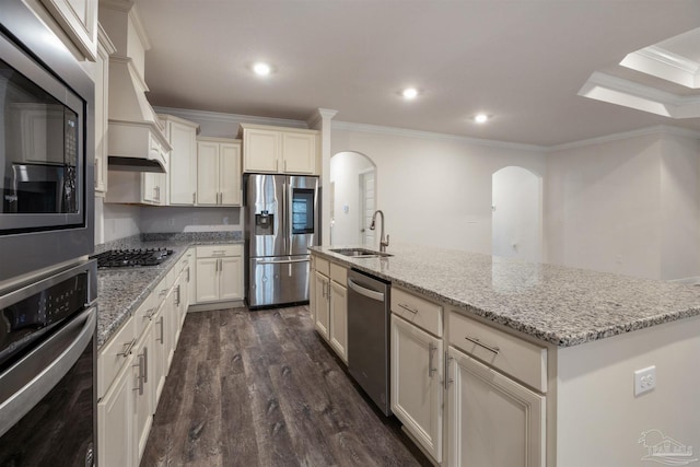 kitchen with stainless steel appliances, sink, light stone countertops, and an island with sink