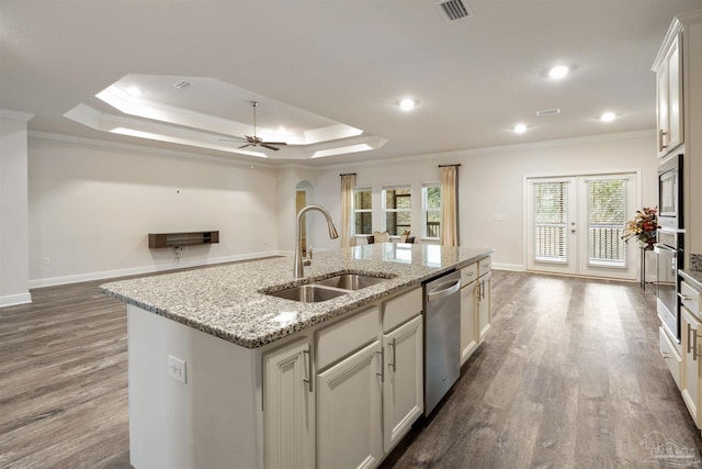 kitchen featuring a raised ceiling, white cabinetry, sink, stainless steel appliances, and a center island with sink