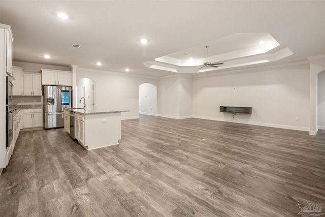 kitchen with appliances with stainless steel finishes, white cabinets, hardwood / wood-style flooring, a kitchen island with sink, and light stone counters