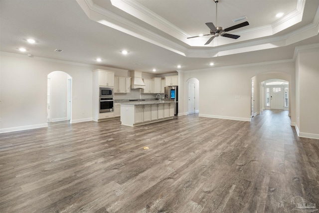 unfurnished living room with a raised ceiling, ceiling fan, crown molding, and light wood-type flooring