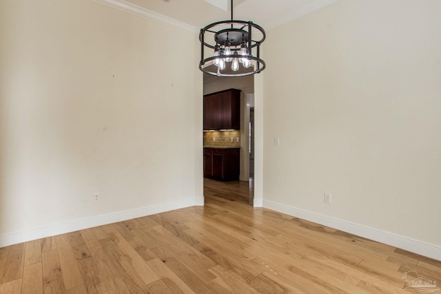 unfurnished dining area with crown molding, an inviting chandelier, and light hardwood / wood-style flooring