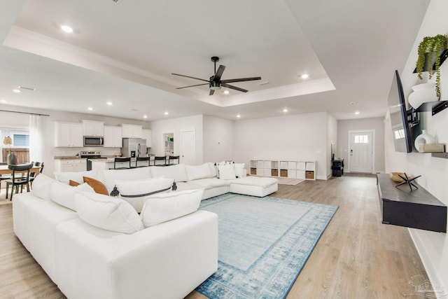 living room with light wood-type flooring, a raised ceiling, and ceiling fan