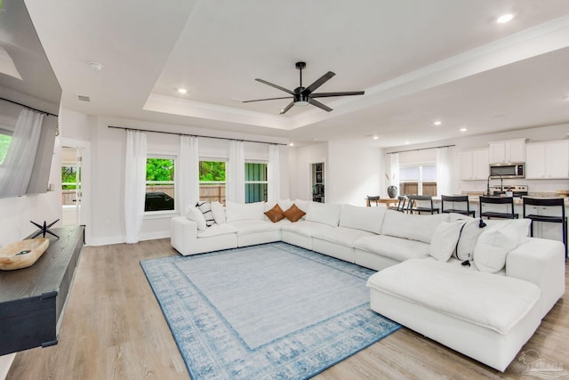 living room featuring plenty of natural light, ceiling fan, light wood-type flooring, and a tray ceiling