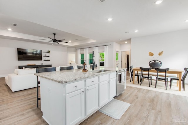 kitchen with white cabinets, light hardwood / wood-style flooring, stainless steel dishwasher, an island with sink, and a breakfast bar area