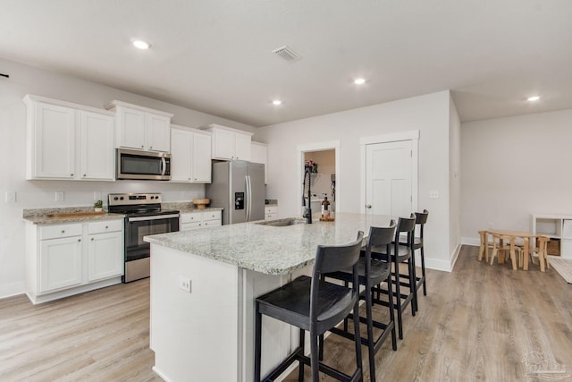 kitchen with a breakfast bar, a center island with sink, appliances with stainless steel finishes, light hardwood / wood-style floors, and white cabinetry