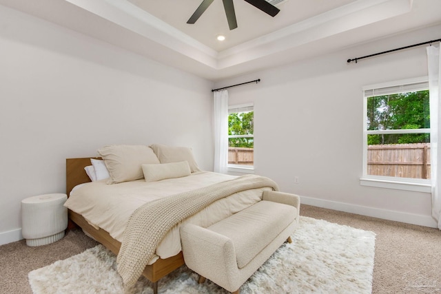 bedroom with light carpet, a tray ceiling, multiple windows, and ceiling fan