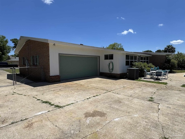view of front of house with fence, an attached garage, brick siding, concrete driveway, and central air condition unit
