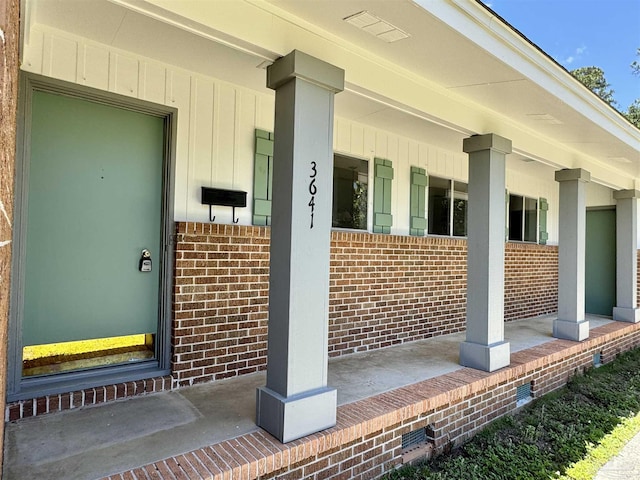 doorway to property with a porch, board and batten siding, and brick siding