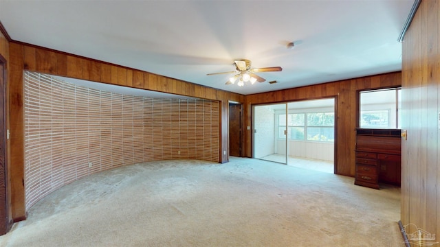 unfurnished bedroom featuring ceiling fan, wood walls, and light colored carpet