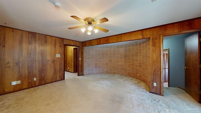 empty room with wood walls, ceiling fan, and light carpet