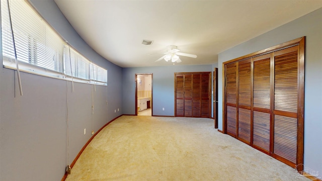 unfurnished bedroom featuring light colored carpet, ensuite bath, a ceiling fan, baseboards, and visible vents