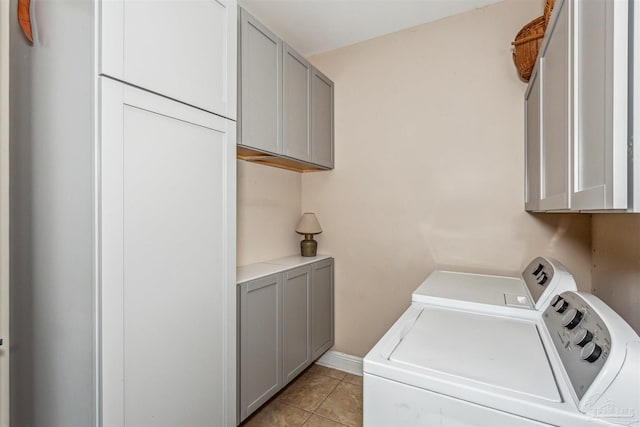 clothes washing area featuring washing machine and dryer, light tile patterned flooring, and cabinets