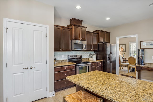 kitchen featuring light tile patterned flooring, dark brown cabinets, backsplash, stainless steel appliances, and light stone countertops