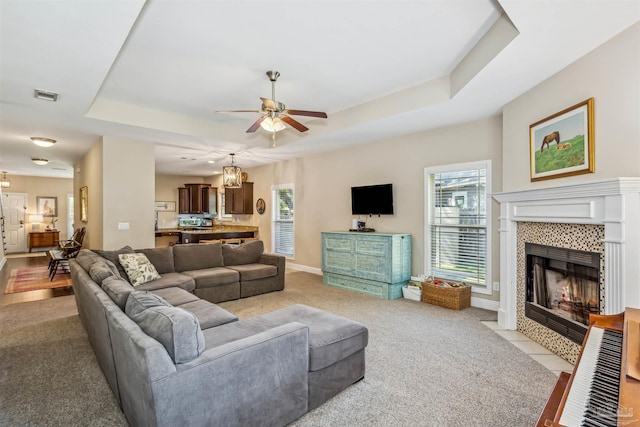 carpeted living room featuring ceiling fan, a tiled fireplace, and a tray ceiling