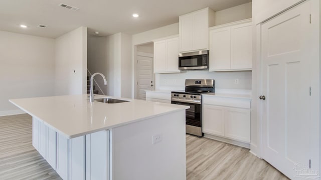 1674 Amaya Ln, Gulf Breeze, FL 32563 - kitchen featuring stainless steel appliances, a sink, light wood-style floors, a center island with sink, and white cabinetry