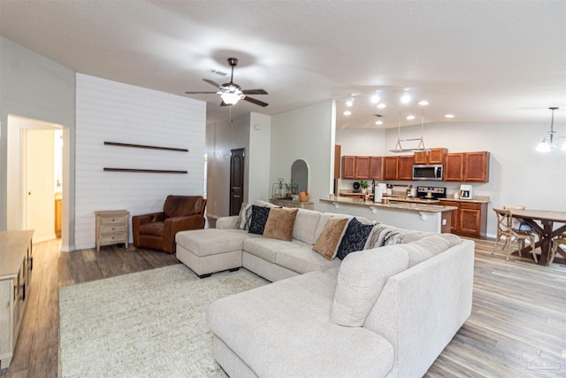 living room with ceiling fan with notable chandelier and light hardwood / wood-style flooring