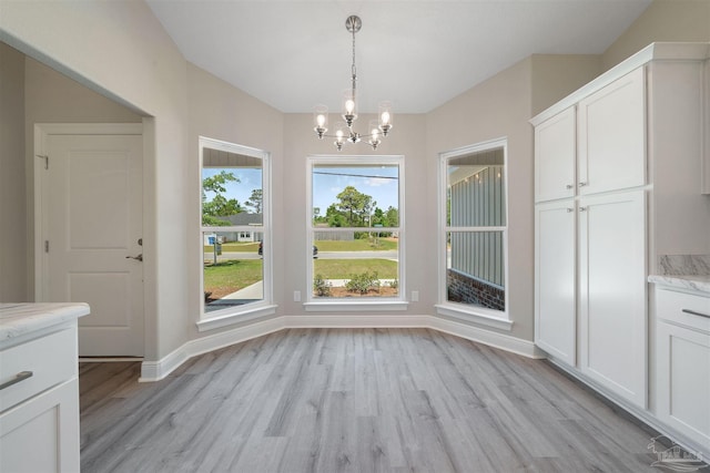 unfurnished dining area with baseboards, a notable chandelier, and light wood finished floors