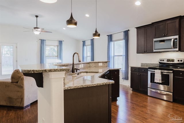 kitchen with pendant lighting, a center island with sink, sink, appliances with stainless steel finishes, and dark brown cabinets