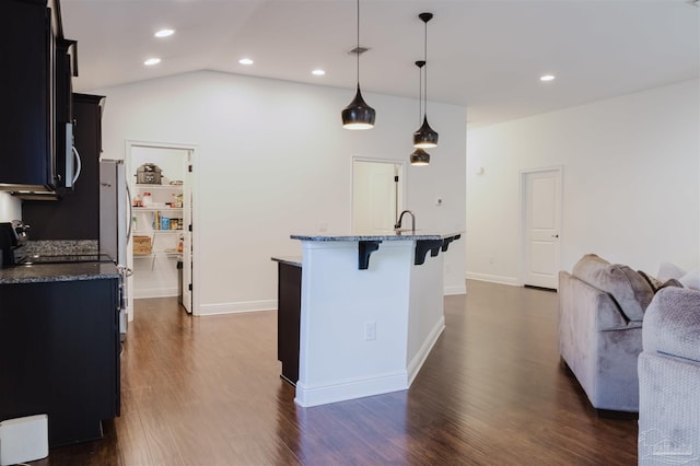 kitchen with a kitchen bar, dark stone counters, decorative light fixtures, a center island with sink, and dark hardwood / wood-style floors