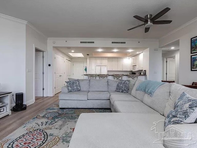 living room featuring hardwood / wood-style flooring, ceiling fan, ornamental molding, and a textured ceiling