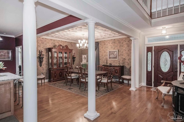 entrance foyer with ornamental molding, wood-type flooring, a chandelier, and decorative columns