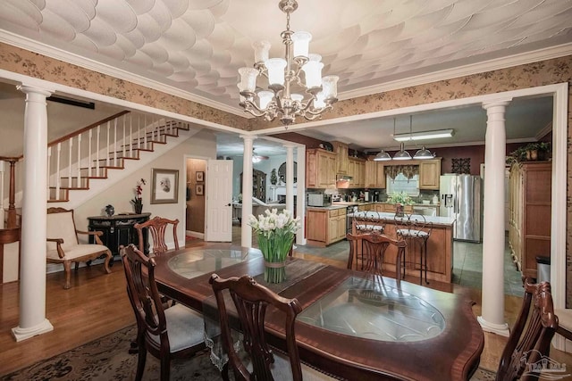 dining space with a notable chandelier, crown molding, light wood-type flooring, and ornate columns