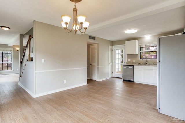 kitchen featuring dishwasher, freestanding refrigerator, white cabinetry, a sink, and a chandelier