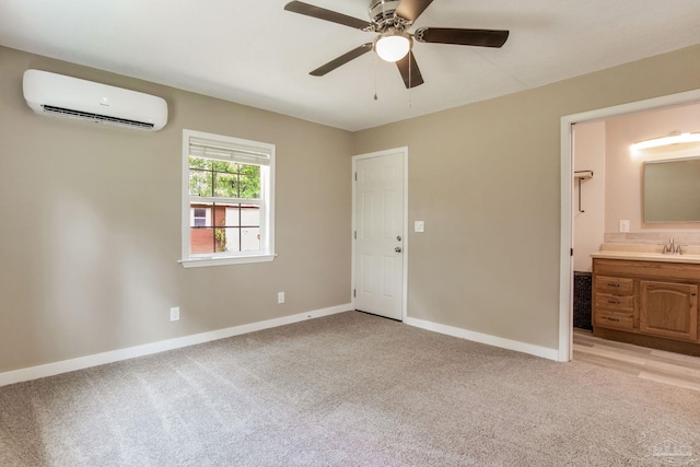 unfurnished bedroom with a wall unit AC, light colored carpet, baseboards, ensuite bath, and a sink