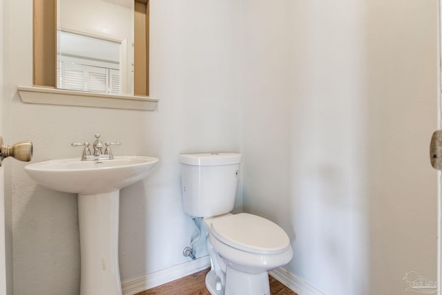 half bathroom featuring toilet, baseboards, wood finished floors, and a sink