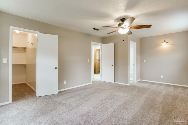 unfurnished bedroom with carpet floors, a walk in closet, baseboards, and a ceiling fan