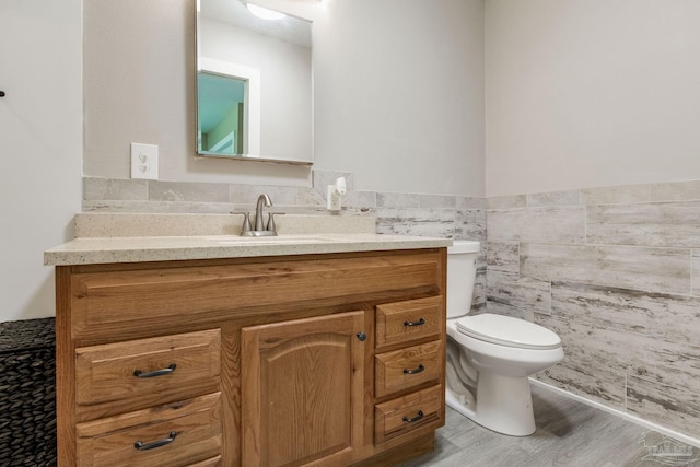 half bathroom with tile walls, toilet, vanity, wainscoting, and wood finished floors