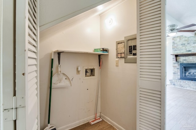 laundry room with hookup for a washing machine, wood finished floors, a glass covered fireplace, a ceiling fan, and baseboards
