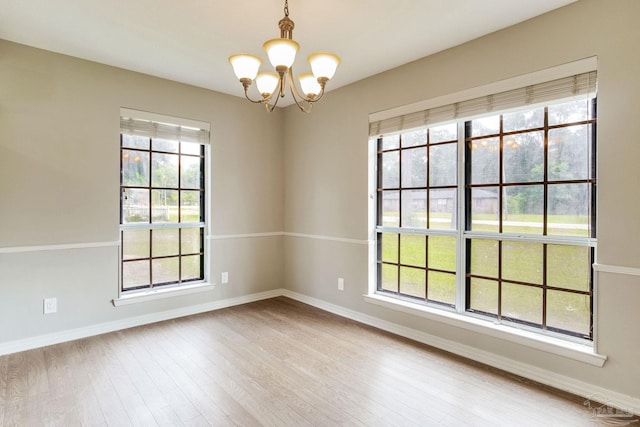 spare room with a chandelier, wood finished floors, and baseboards