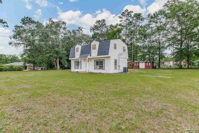 rear view of property with a gambrel roof, roof with shingles, a yard, and an outbuilding