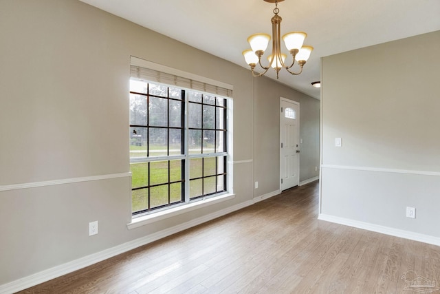 spare room featuring a chandelier, wood finished floors, and baseboards