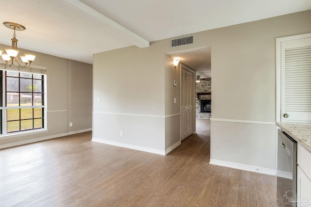 spare room featuring light wood-type flooring, a chandelier, baseboards, and a large fireplace