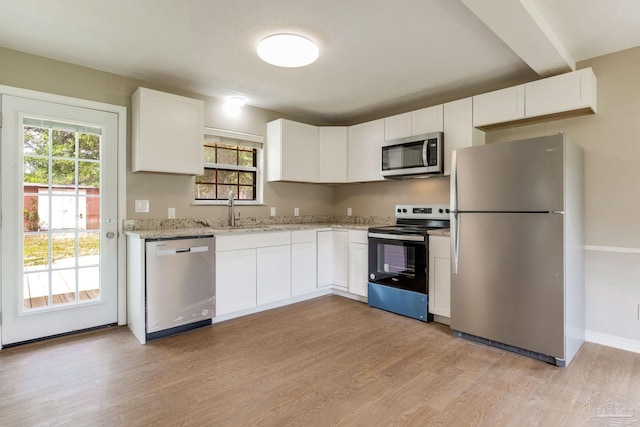 kitchen featuring appliances with stainless steel finishes, a sink, light wood-style floors, light stone countertops, and white cabinetry