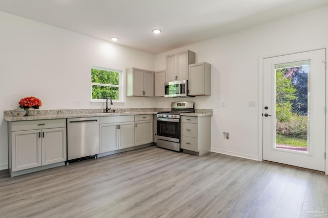 kitchen featuring light hardwood / wood-style floors, gray cabinets, light stone counters, sink, and stainless steel appliances