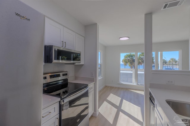 kitchen with stainless steel appliances, sink, white cabinets, and light wood-type flooring