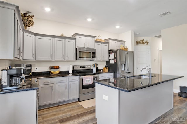 kitchen featuring a center island with sink, hardwood / wood-style floors, sink, stainless steel appliances, and dark stone counters