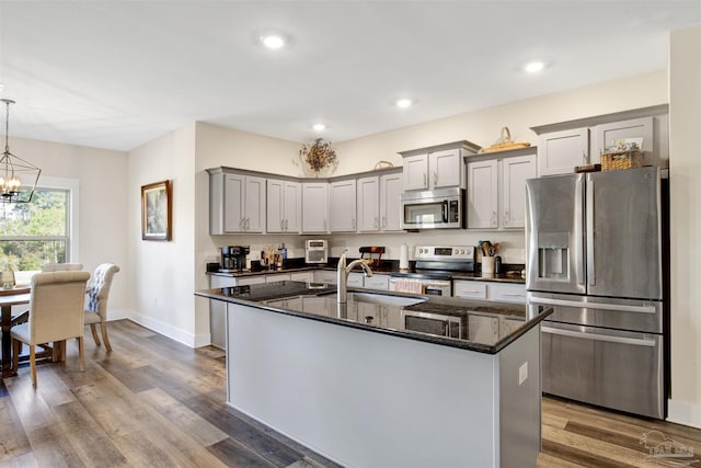 kitchen with appliances with stainless steel finishes, decorative light fixtures, dark stone counters, an island with sink, and a chandelier