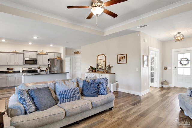 living room with sink, ceiling fan with notable chandelier, ornamental molding, and hardwood / wood-style floors