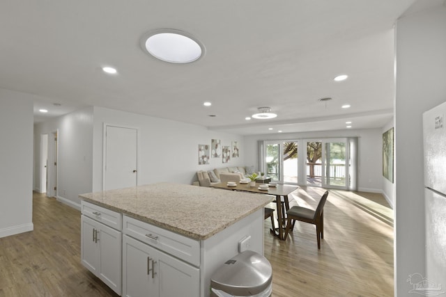 kitchen with light stone counters, a kitchen island, white cabinets, and light wood-type flooring