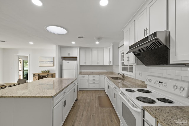 kitchen with white appliances, a center island, light stone counters, white cabinets, and light wood-type flooring