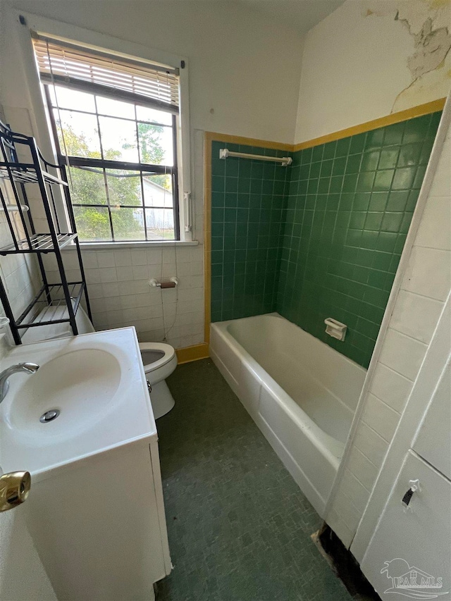 full bathroom featuring toilet, tiled shower / bath combo, vanity, and tile walls