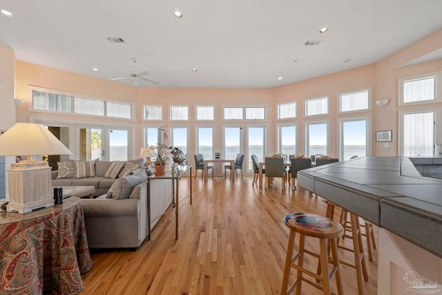 living room featuring light wood-type flooring, french doors, ceiling fan, and a water view